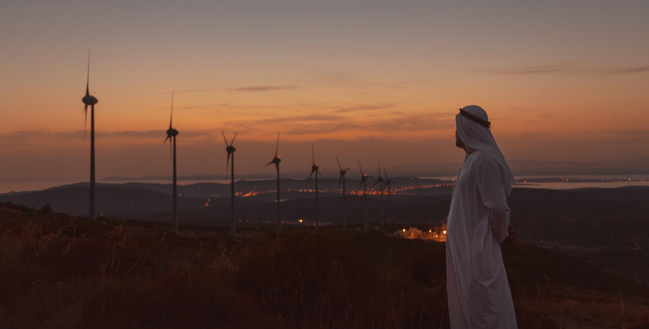 Middle Eastern man on the wind turbine farm at sunset
