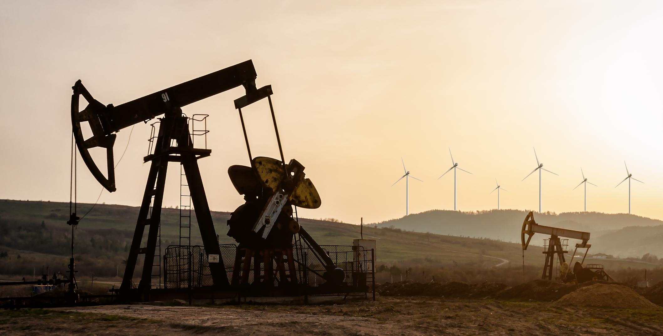 Oil pumps and wind turbines at sunset